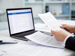 Solicitor comparing marked-up contract pages beside a laptop in a calm office